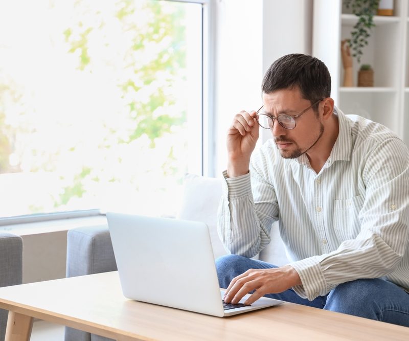 Man researching EVO ICL pricing and treatment costs on a laptop while at home, learning how much is evo icl – how much is evo icl